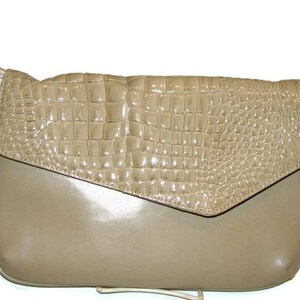 Peut inclure: Un sac à bandoulière en cuir beige gaufré crocodile avec une fermeture à rabat. Le sac a une finition en cuir lisse et une longue bandoulière.
