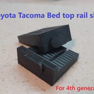 May include: Black Toyota Tacoma bed top rail shims. The image shows two black, rectangular shims with a textured surface and rounded edges. Text in the image reads "Toyota Tacoma Bed top rail shim" and "For 4th generation Tacoma."