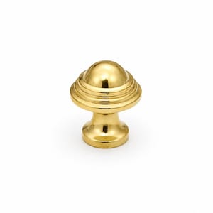 Peut inclure: Un bouton de meuble en laiton poli doté d'un sommet bombé lisse et de stries circulaires concentriques autour de la base. La quincaillerie présente une finition métallique réfléchissante et un pied évasé qui se rétrécit avant de s'élargir.