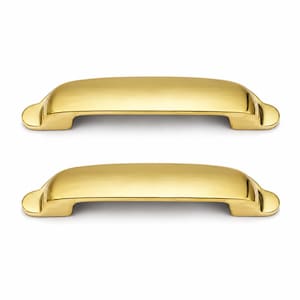May include: Two polished brass cabinet pulls with a smooth, arched design. Each handle features a rounded, elongated top surface that curves downward at both ends, terminating in flat, circular mounting points for attachment to furniture.
