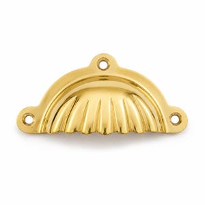 May include: A polished gold-tone metal cup pull handle featuring a semi-circular shell-inspired design with vertical fluted ridges. The hardware includes three circular mounting holes, one at the top center and two on the side extensions.