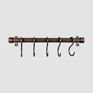Puede incluir: Un riel de metal de color bronce oscuro para montaje en pared, con una varilla cilíndrica, dos tapas en los extremos y dos soportes de montaje rectangulares. Cinco ganchos en forma de S a juego cuelgan de la varilla para colgar objetos.