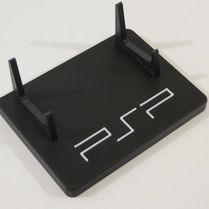 Peut inclure: Support noir pour console PSP avec logo PSP blanc. Le support possède deux supports verticaux et une base rectangulaire. Conçu pour maintenir une console PSP.