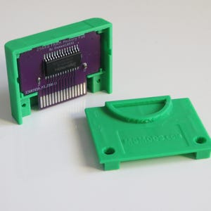 May include: Green plastic case for a 256Kb Flash RAM Memory Pak for the Game Boy Color. The case is open and the circuit board is visible. The text on the circuit board reads "256Kb Flash RAM Memory Pak By Element1420".