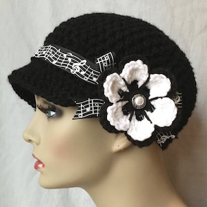 May include: Black crochet beanie with a black and white musical note ribbon and a white crochet flower with a pearl button in the center.