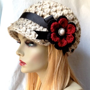 May include: A beige crocheted hat with a black ribbon and a red and black crocheted flower with a pearl button in the center.
