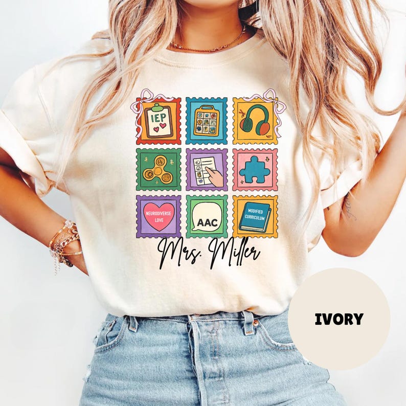 May include: Ivory-colored t-shirt featuring a colorful stamp design with various icons and text, including "IEP," a puzzle piece, and "AAC." The shirt also has the text "Mrs. Miller" in a script font.