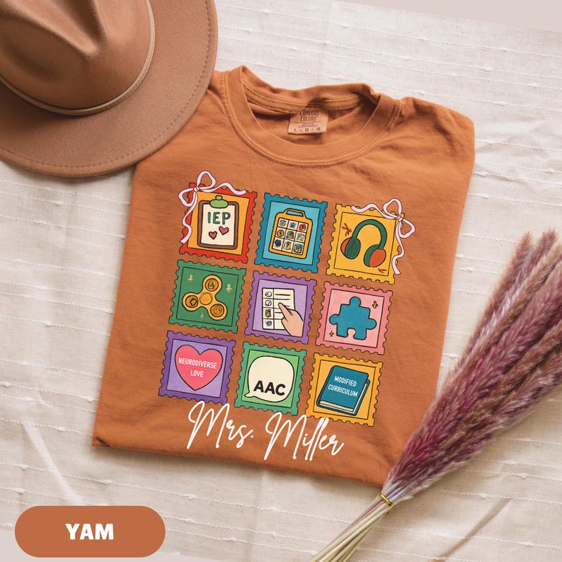 May include: A burnt orange t-shirt featuring a colorful stamp design with various icons and the text "Mrs. Miller". The stamps include images of a heart, headphones, a puzzle piece, and a fidget spinner. A brown hat and decorative plant are in the background.