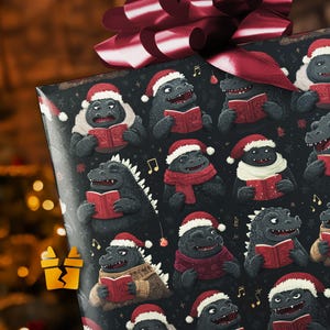 May include: Christmas-themed gift wrap featuring a repeating pattern of cartoon Godzilla-like monsters wearing Santa hats and reading books. The monsters are in various outfits, including scarves and sweaters, against a black background with musical notes.