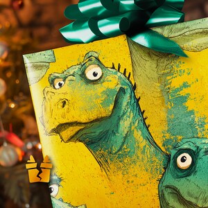 May include: A wrapped gift with a green bow. The wrapping paper features a cartoon illustration of a green dinosaur on a yellow background. The dinosaur has large eyes and a friendly expression. The gift is likely for a holiday or special occasion.