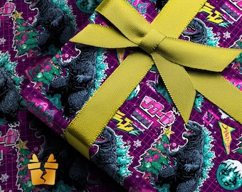 Puede incluir: Una caja de regalo envuelta con papel de regalo morado con un patrón de Godzilla y árbol de Navidad. El regalo está atado con una cinta dorada. El papel de regalo tiene un patrón de cuadrícula.