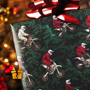 Op de afbeelding: Cadeaupapier met een herhalend patroon van motorcrossers in rode en witte uitrusting op crossmotoren. De achtergrond is donkergroen met een kerstboomontwerp. Een grote rode strik siert de bovenkant van het ingepakte cadeau.