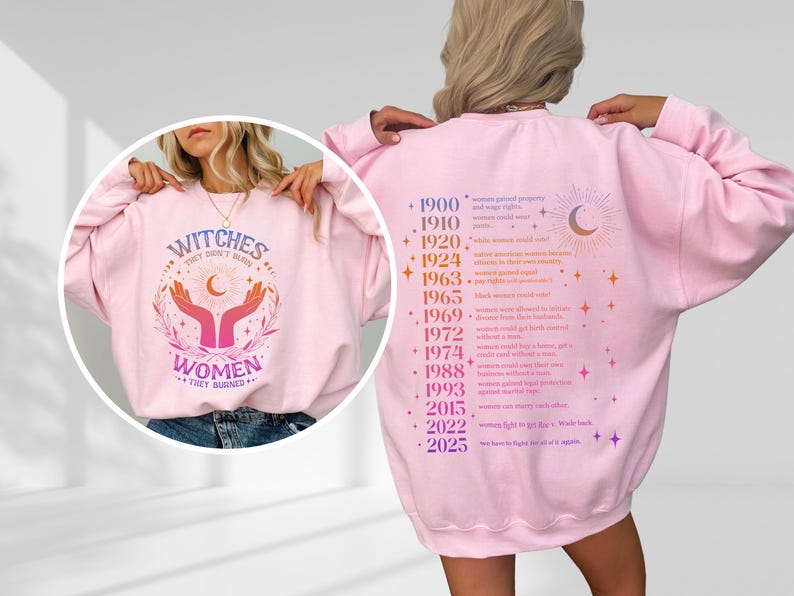 May include: Pink sweatshirt with a graphic print of hands holding a crescent moon and stars. The text "Witches They Don't Burn Women They Burned" is printed on the front. The back of the sweatshirt has a list of historical events related to women's rights.