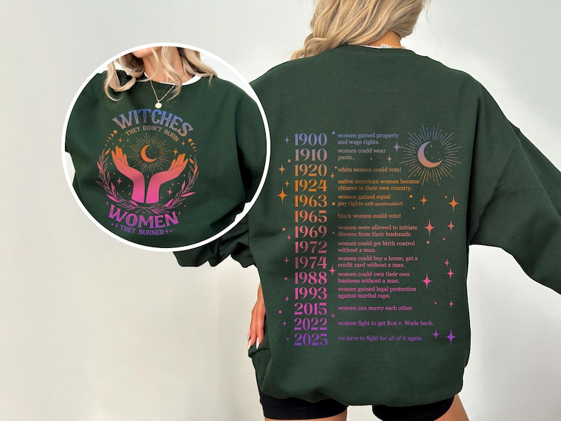 May include: Green sweatshirt with a graphic print of a crescent moon and stars on the back. The front of the sweatshirt has a graphic print of two hands reaching up to a crescent moon with the text "Witches They Don't Burn Women They Rise" in a rainbow gradient.