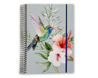 May include: A gray spiral bound notebook with a blue ribbon bookmark. The cover features a watercolor illustration of a hummingbird flying near pink and red hibiscus flowers.
