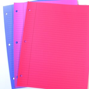 May include: Three sheets of lined paper in blue, pink, and magenta. Each sheet has three holes for binder storage. The paper is arranged on a white surface, creating a visually appealing contrast.