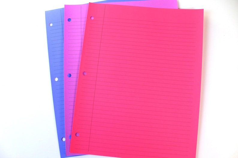 May include: Three sheets of lined paper in blue, pink, and magenta. Each sheet has three holes for binder storage. The paper is arranged on a white surface, creating a visually appealing contrast.