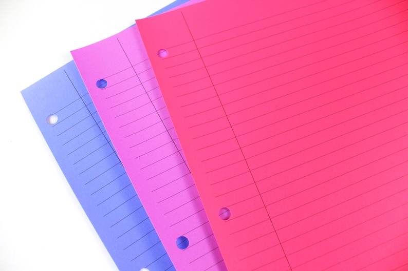May include: Three sheets of lined paper in shades of blue, pink, and red. Each sheet has three holes for binder use. The paper is arranged diagonally, with the colours overlapping.