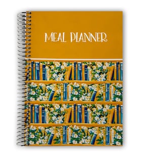 May include: Spiral-bound meal planner with a mustard yellow cover and the words "MEAL PLANNER" in white script. The lower portion features a repeating pattern of bookshelves with blue and yellow books and white floral accents.