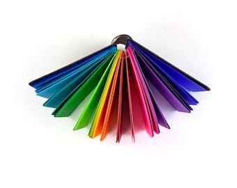 May include: A rainbow-colored swatch book with pages fanned out. The pages are arranged in a spectrum of colors, from red to violet, and bound together with a metal ring. The background is plain white.