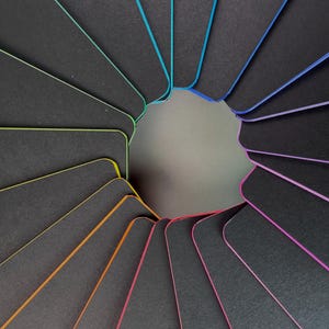 May include: A set of black cards with colorful edges arranged in a circle. The edges are in a rainbow pattern.