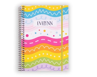 May include: A spiral-bound notebook featuring a colorful pattern of horizontal wavy lines in yellow, blue, pink, orange, and green. The cover includes white polka dots and scribbles, with the name EVELYNN printed in a central white rectangular box.