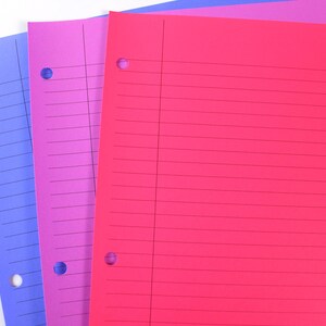 May include: A stack of three colourful, lined paper sheets. The sheets are in shades of blue, purple, and red. Each sheet has three holes along the left edge for binder storage. The paper is blank and ready for notes.