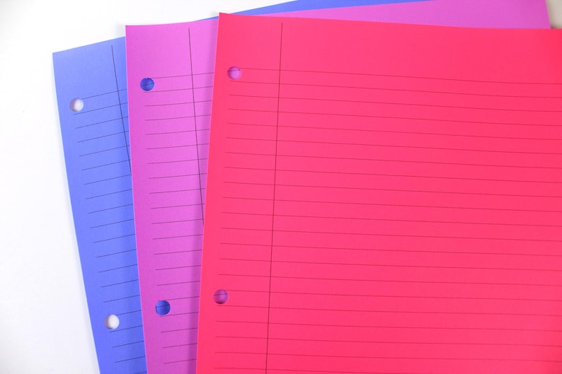 May include: A stack of three colourful, lined paper sheets. The sheets are in shades of blue, purple, and red. Each sheet has three holes along the left edge for binder storage. The paper is blank and ready for notes.