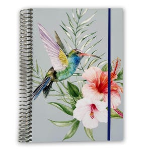 May include: A gray spiral bound notebook with a blue ribbon bookmark. The cover features a watercolor illustration of a hummingbird in flight with green, blue, and yellow feathers, surrounded by pink and white hibiscus flowers and green leaves.