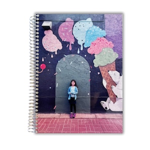 May include: Spiral-bound notebook featuring a colorful mural of an ice cream cone with polar bears and dripping ice cream scoops in pink, blue, and green. A person stands in front of the mural.