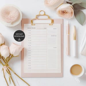 May include: A pink daily planner with a gold clip,  "DAILY PLAN" printed at the top, and sections for "DATE", "NOTES", "PRIORITIES", and "TO DO". The planner is on a white surface with a cup of coffee, pens, and flowers.