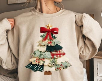 Può includere: Felpa beige con un design ad albero di Natale patchwork. L'albero è adornato con un fiocco rosso, una stella dorata e vari motivi di tessuto, tra cui floreale, pois e scozzese. Un capo d'abbigliamento festivo e accogliente.