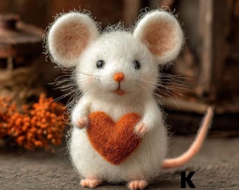 Puede incluir: Una figura de ratón hecha a mano de fieltro blanco con orejas grandes y esponjosas y una pequeña nariz naranja. El ratón sostiene un corazón de fieltro en tonos naranja. La cola es de color rosa claro. La letra "K" es visible en la esquina inferior derecha.