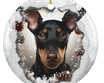 Könnte beinhalten: Runder Weihnachtsbaumschmuck aus Keramik mit einem schwarz-braunen Hund, der aufmerksam in die Kamera blickt. Der Hund wird von einem schneebedeckten Rand mit Tannenzapfen umrahmt. Ein goldener Faden zum Aufhängen.