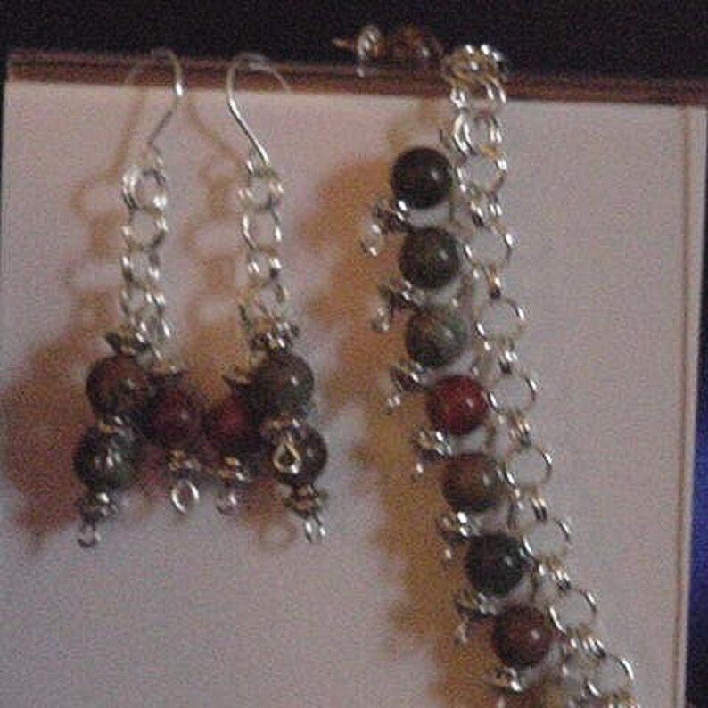 Peut inclure: Un ensemble de boucles d'oreilles en cha&icirc;ne argent&eacute;e et un bracelet assorti avec des perles de pierres pr&eacute;cieuses vertes, brunes et rouges.