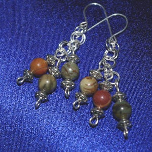 Peut inclure: Boucles d'oreilles en cha&icirc;ne argent avec plusieurs perles de pierres pr&eacute;cieuses brunes, rouges et vertes.