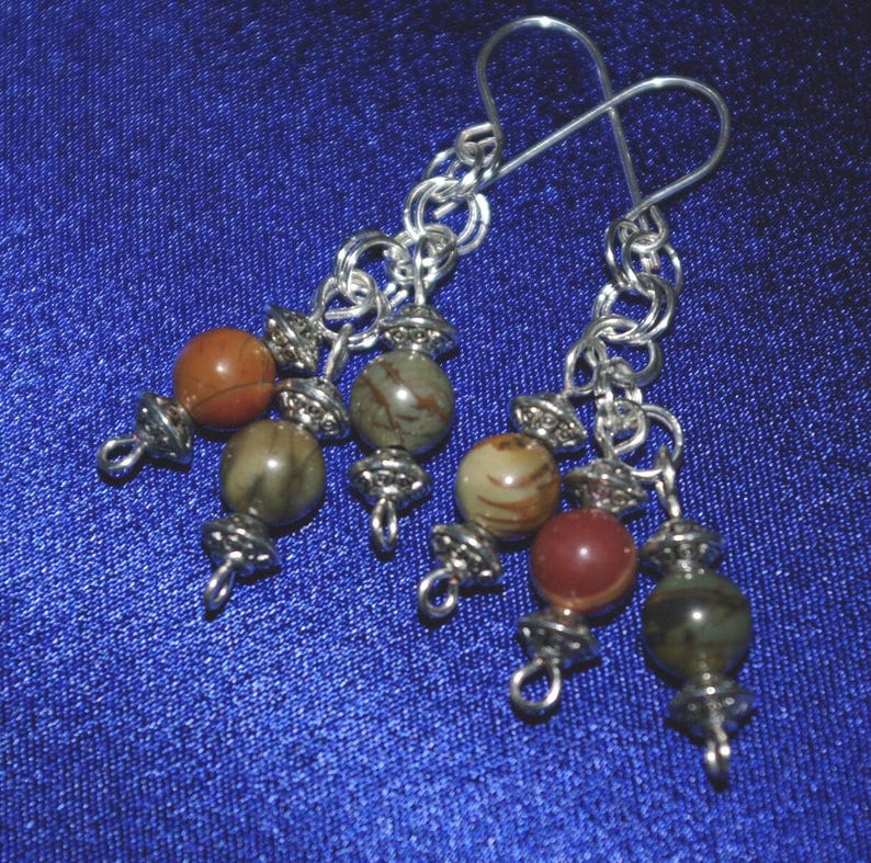 Peut inclure: Boucles d'oreilles en cha&icirc;ne argent avec plusieurs perles de pierres pr&eacute;cieuses brunes, rouges et vertes.