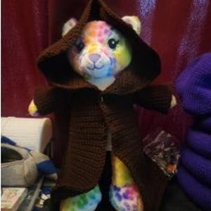 May include: A colorful stuffed animal wearing a brown crocheted hooded robe.