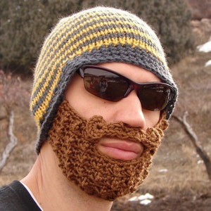 May include: A person wearing a grey and yellow striped knitted hat with a brown crocheted beard attached.