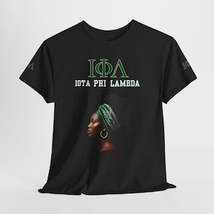 Könnte beinhalten: Schwarzes T-Shirt mit dem Text "IOTA PHI LAMBDA" in Grün und Weiß. Das Shirt hat eine Grafik einer Frau, die ein grün-weißes Kopftuch trägt. Auf dem linken Ärmel befinden sich auch grüne griechische Buchstaben.