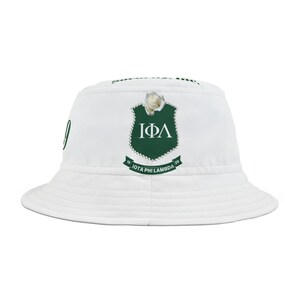 Pode incluir: Chapéu bucket branco com um brasão verde com as letras gregas IΦΛ e uma rosa branca. O chapéu também tem o texto "IOTA PHI LAMBDA" e os números "19" e "29".