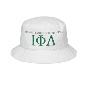 May include: White bucket hat featuring the text "IOTA PHI LAMBDA SORORITY, INC." in green, along with the Greek letters "ΙΦΛ". The hat has a wide brim and a rounded crown, suitable for sun protection.
