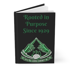 Può includere: Diario nero con la scritta "Rooted in Purpose Since 1929" in verde. La copertina presenta un disegno verde e bianco con le lettere "ΙΦΛ" e una rosa. Il diario è un taccuino.