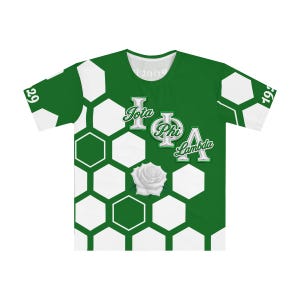 以下が含まれることがあります： 緑と白の半袖Tシャツで、ハニカム模様が繰り返されています。中央には、白いバラのグラフィックの上に白と銀の文字で「Iota Phi Lambda」と書かれています。袖には数字の19と29がデザインされています。