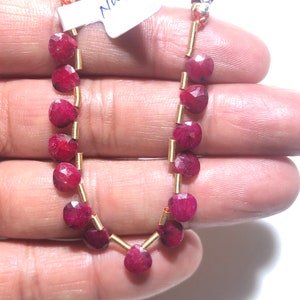 May include: A strand of ruby gemstone beads with gold spacers. The beads are faceted and have a deep red color.