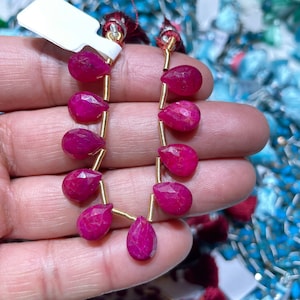 May include: A strand of ruby red gemstone beads strung on gold wire. The beads are pear shaped and have a faceted finish.
