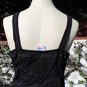 May include: Black tank top with thin straps and decorative lace trim. The top has a square neckline and a tag that reads "intimately free people". The fabric appears to be a lightweight material.