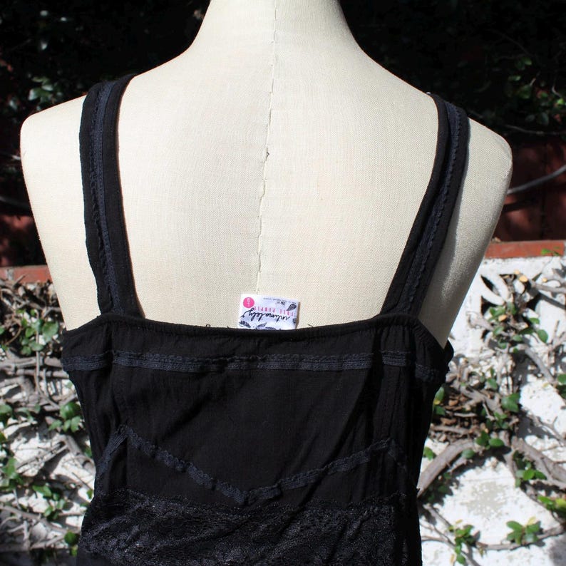 May include: Black tank top with thin straps and decorative lace trim. The top has a square neckline and a tag that reads "intimately free people". The fabric appears to be a lightweight material.