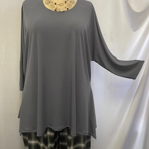 May include: A gray, long-sleeved, loose-fitting top with a round neckline. The top is made of a soft, flowing fabric and has a slightly A-line shape. The top is paired with black and white plaid pants.