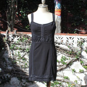 May include: A black dress with spaghetti straps and a fitted bodice. The dress features lace detailing across the chest and hemline, with vertical seams adding structure. The dress is displayed on a mannequin.